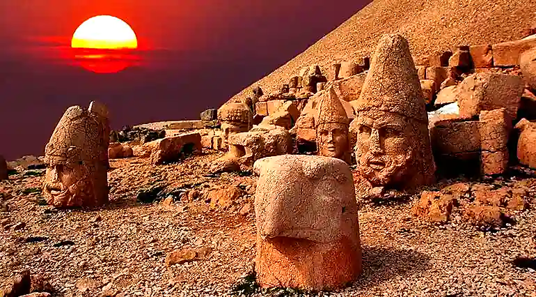 Sunset at Mount Nemrut: The sun descends behind the iconic stone heads, casting a warm glow across the ancient mountaintop sanctuary. 