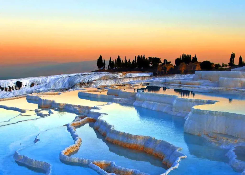 Sunset view of Pamukkale travertines, with the white terraces glowing orange in the warm light of the setting sun.